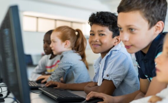 Five students at a primary school happily learning on reliable computers and IT equipment in a classroom benefitting from outsourced it support for schools including theirs