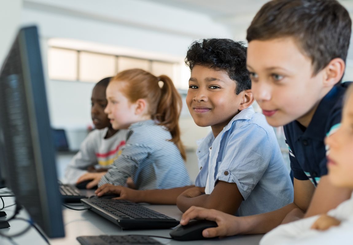 Five students at a primary school happily learning on reliable computers and IT equipment in a classroom benefitting from outsourced it support for schools including theirs