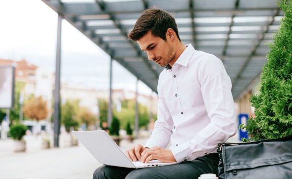 A remote worker uses a laptop in a public outdoor space, emphasising the potential risks associated with connecting to public Wi-Fi networks.